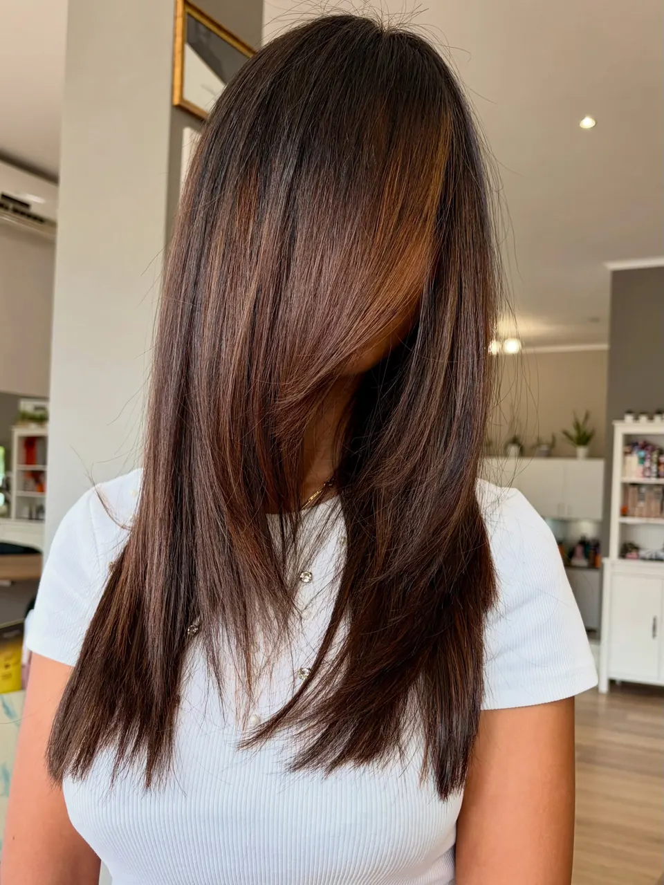 Taglio lungo scalato su capelli castani con riflessi rame.