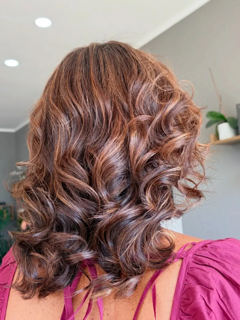 Capelli castani con riflessi ramati e ricci definiti, visti da dietro.